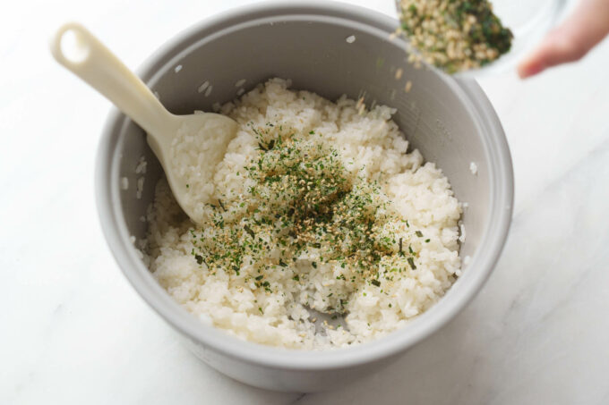 sprinkling furikake into cooked rice pot