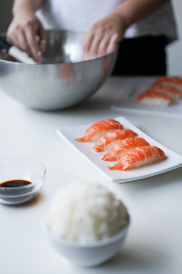 four salmon nigiri ready to eat, with bowl of sushi rice and soy sauce